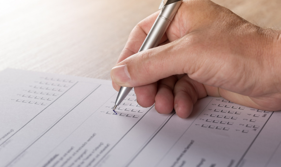 Zdjęcie dłoni trzymającej długopis i wypełniającej ankietę