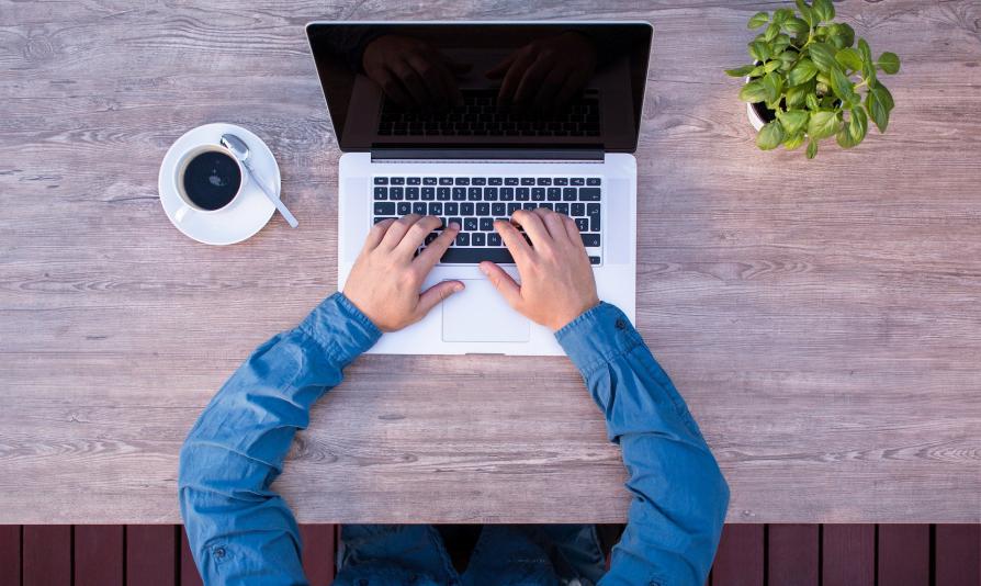 Męskie ręce przy biurku wciskają klawisze laptopa (fotografia)