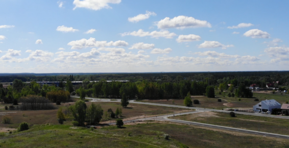 Widok ulicy Przelot i Świdnickiej w Toruniu z lotu ptaka. Asfaltowa droga pośród łąki. Na horyzoncie las i budynki