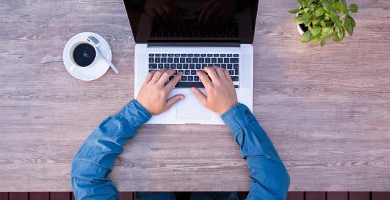 Męskie ręce przy biurku wciskają klawisze laptopa (fotografia)