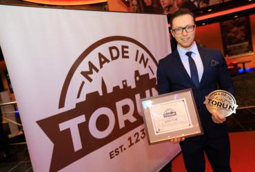 Laureat znaku pozuje z certyfikatem na tle banera z logiem Made in Toruń